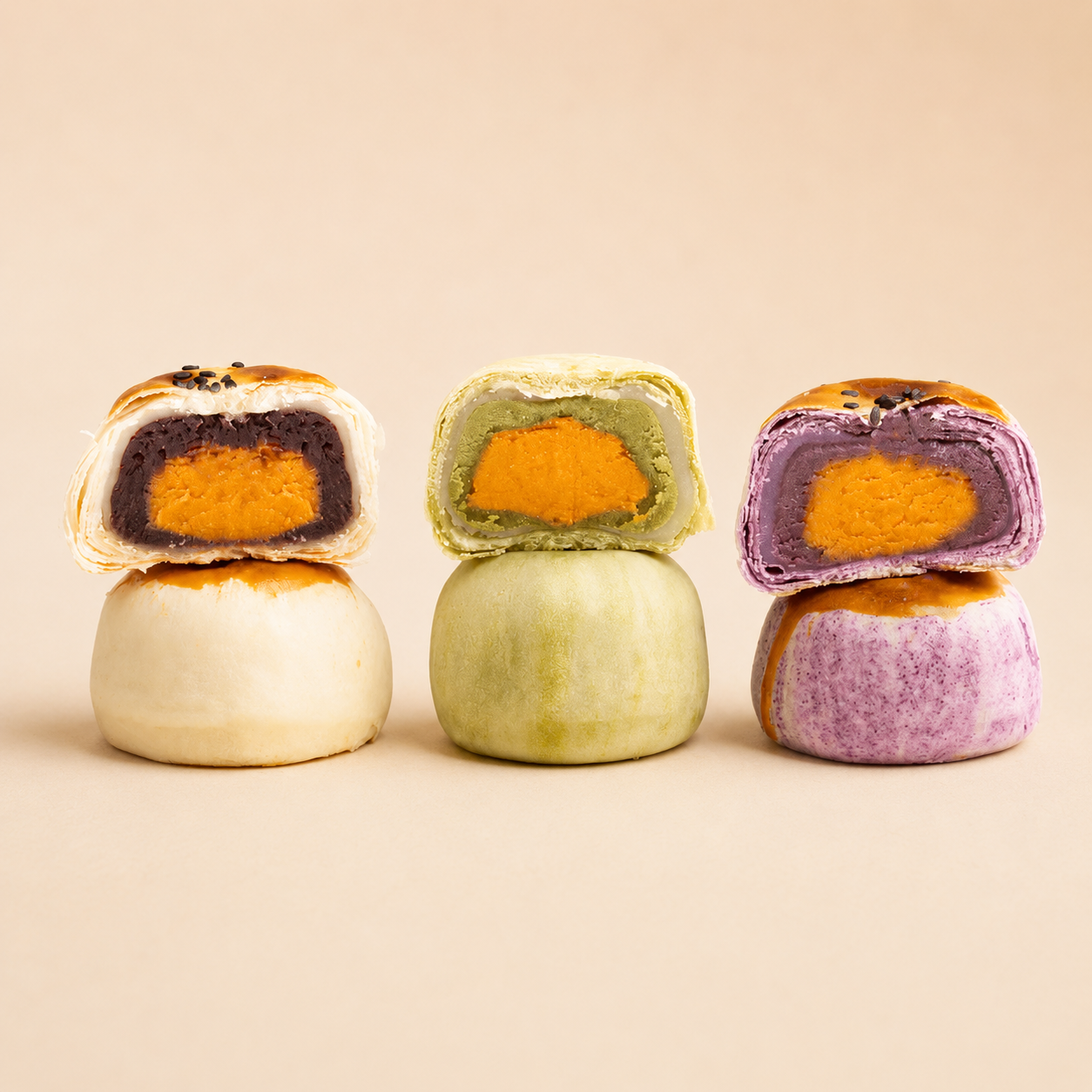 Three colorful sweet pastries stacked on a beige background, each cut in half to show a vibrant salted eggyolk filling. The left pastry has a red beans filling, the middle has a matcha filling, and the right has a taro filling.