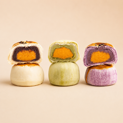 Three colorful sweet pastries stacked on a beige background, each cut in half to show a vibrant salted eggyolk filling. The left pastry has a red beans filling, the middle has a matcha filling, and the right has a taro filling.